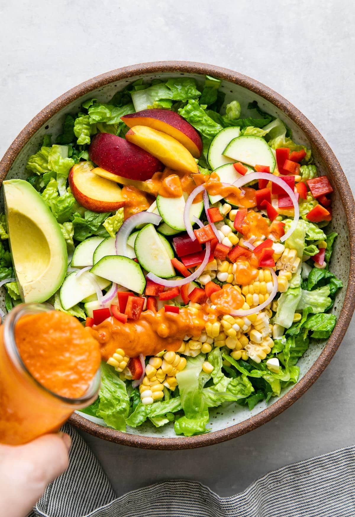 top down view of sun-dried tomato dressing being poured overtop farmer's market salad.