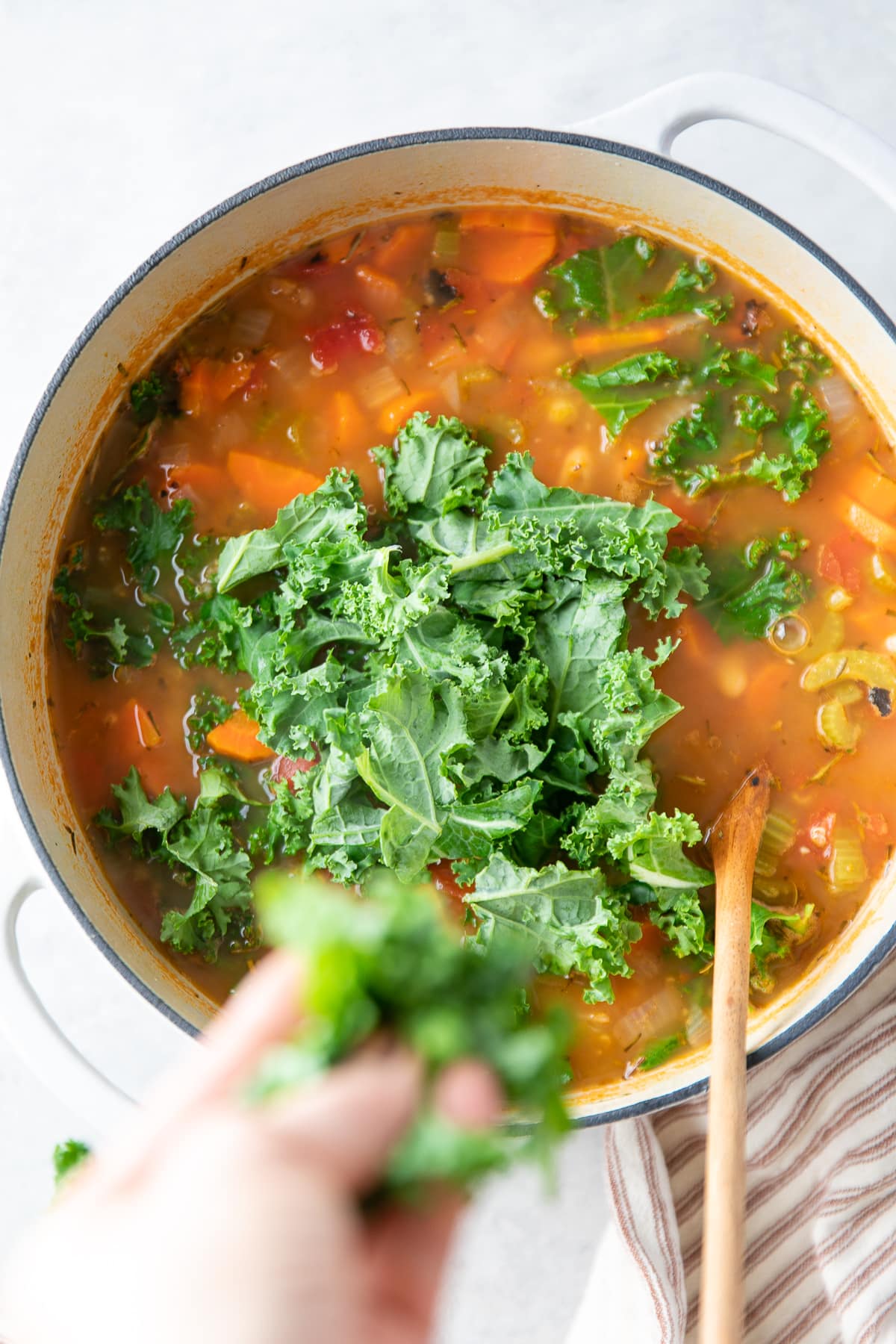 top down view of chopped kale being added to pot of hot soup.