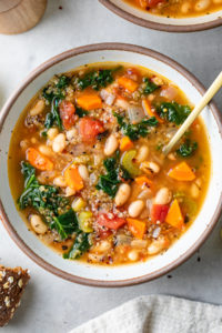 top down view of bowl with serving of kale, quinoa and white bean soup with spoon.