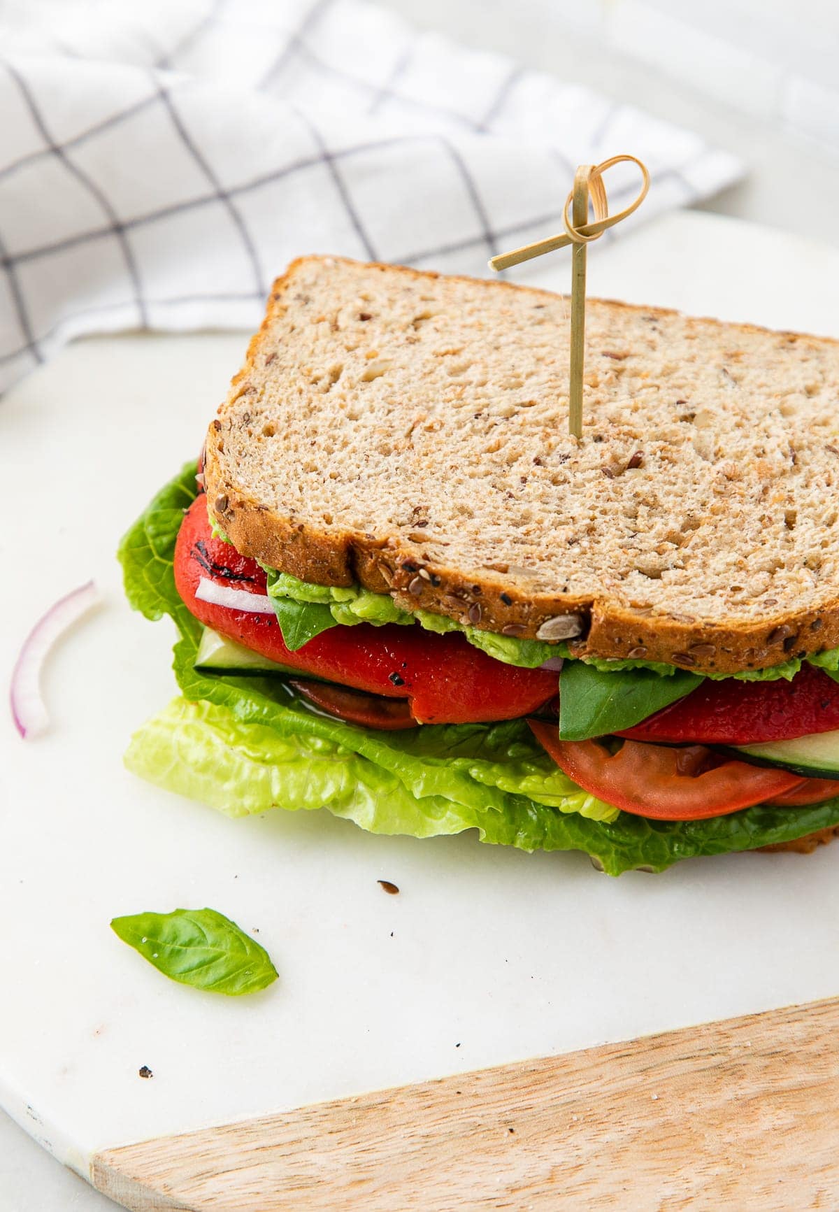 side angle view of sliced and stacked mediterranean veggie sandwich with red peppers on a marble serving tray.