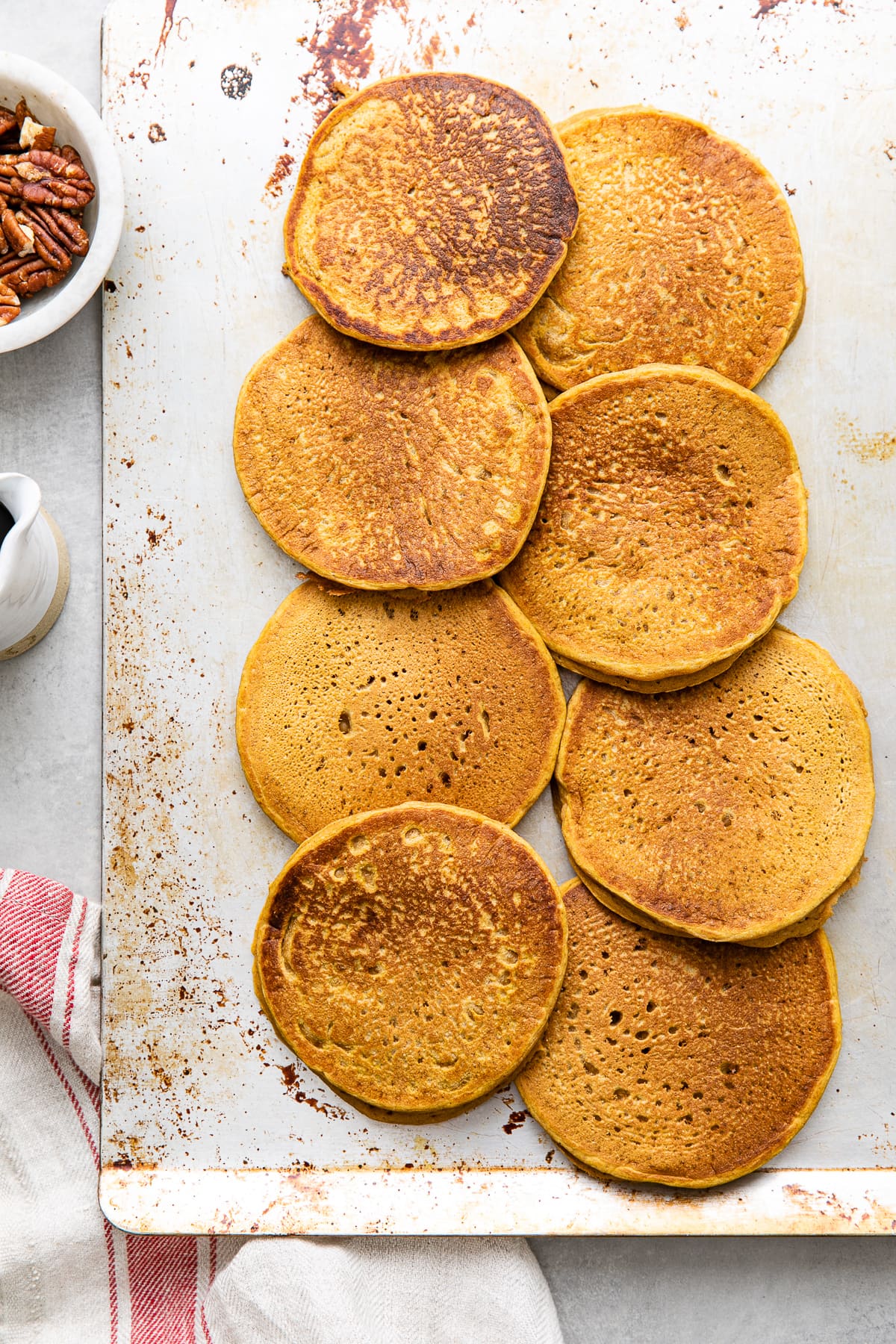 top down view of freshly made vegan pumpkin pancakes keeping warm on a baking sheet.