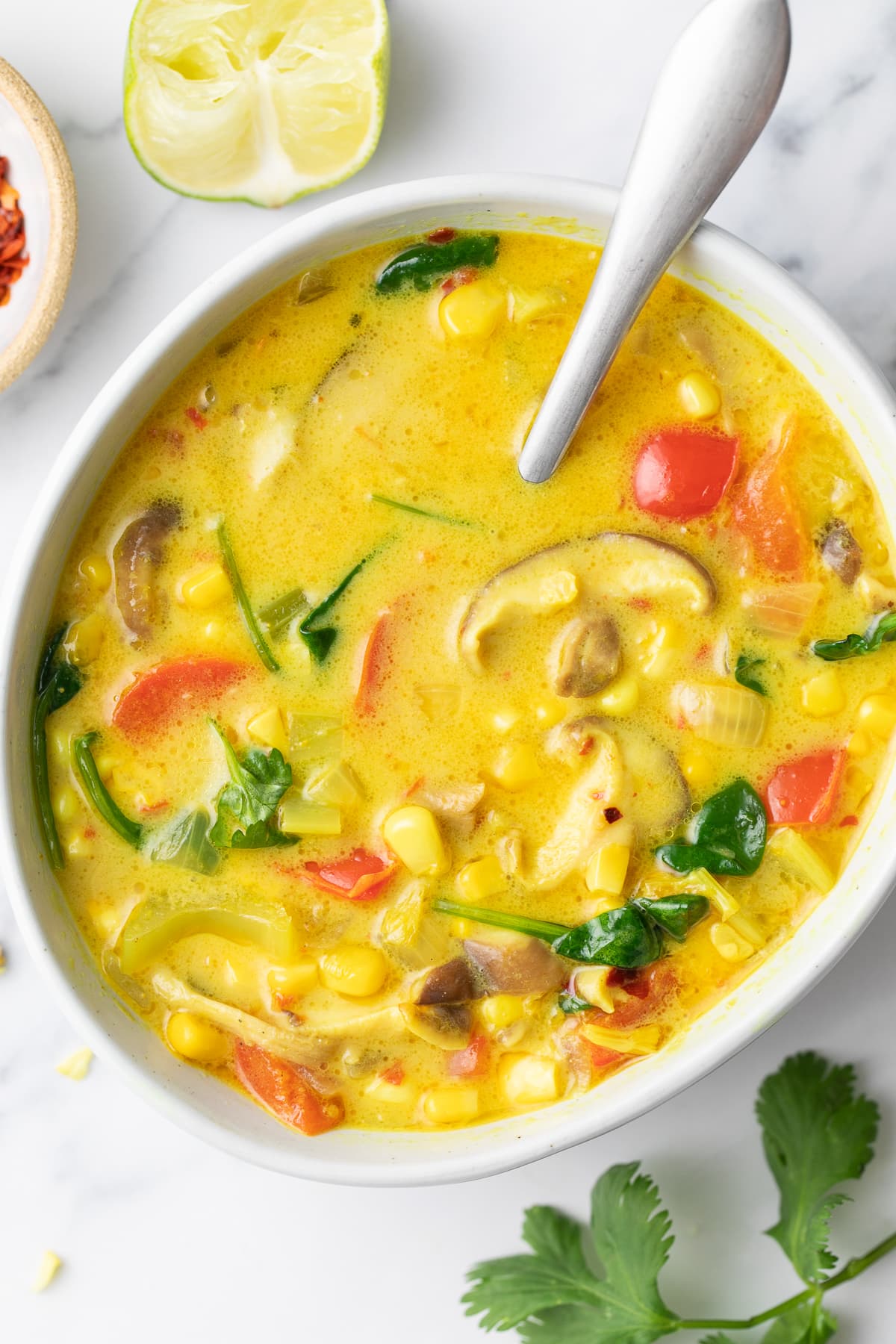 top down view of plated thai coconut curry corn soup with items surrounding.