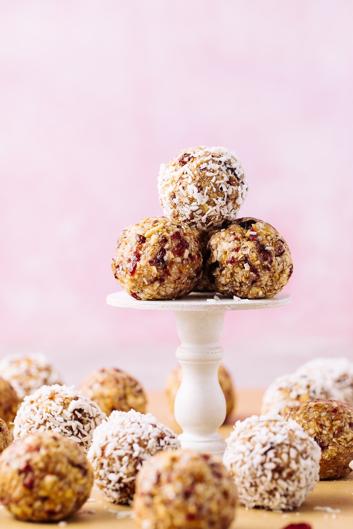 head on view of group of vegan cranberry energy bites on a cupcake stand with items surrounding.