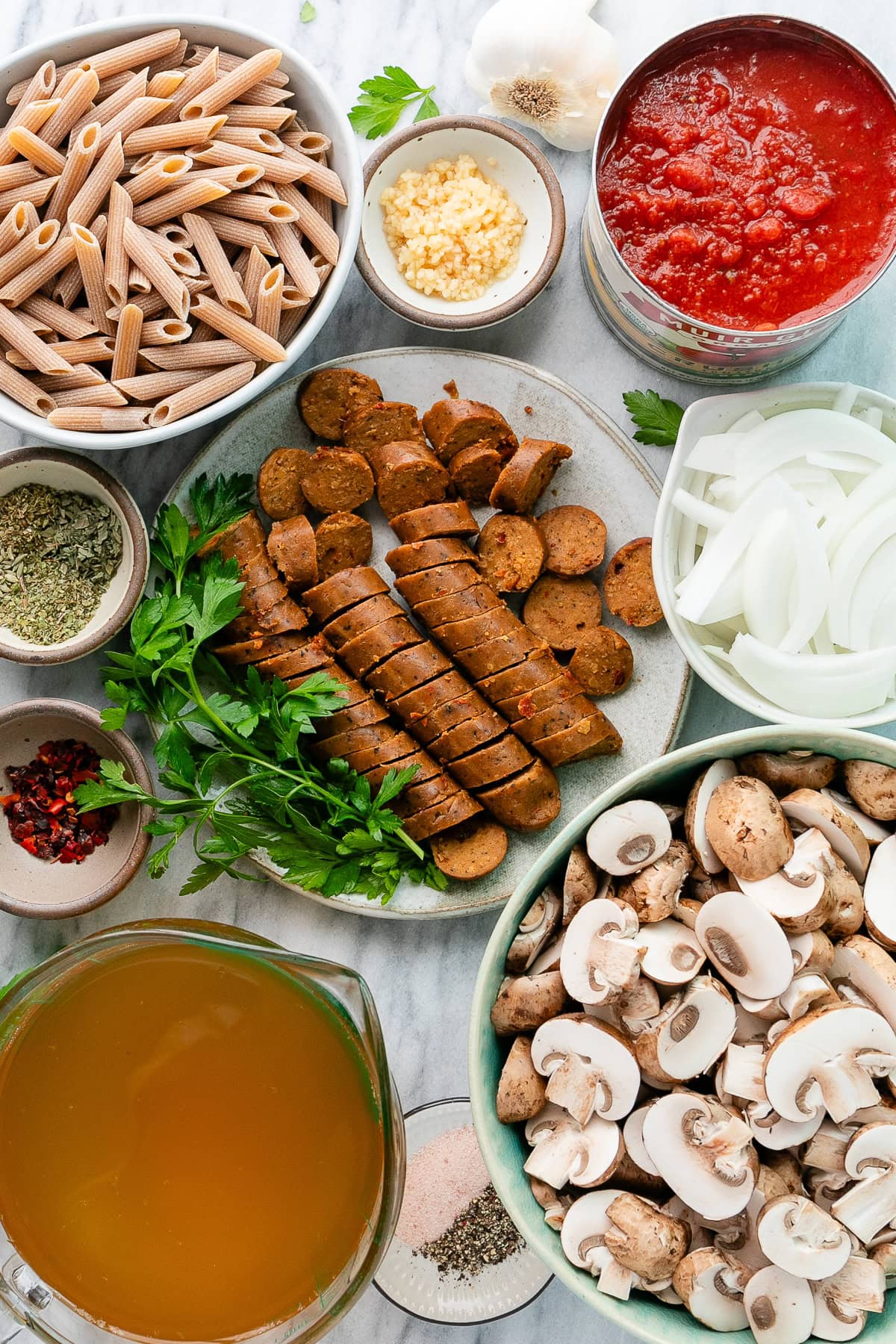top down view of ingredients used to make one pot vegan sausage pasta on a marble slab.