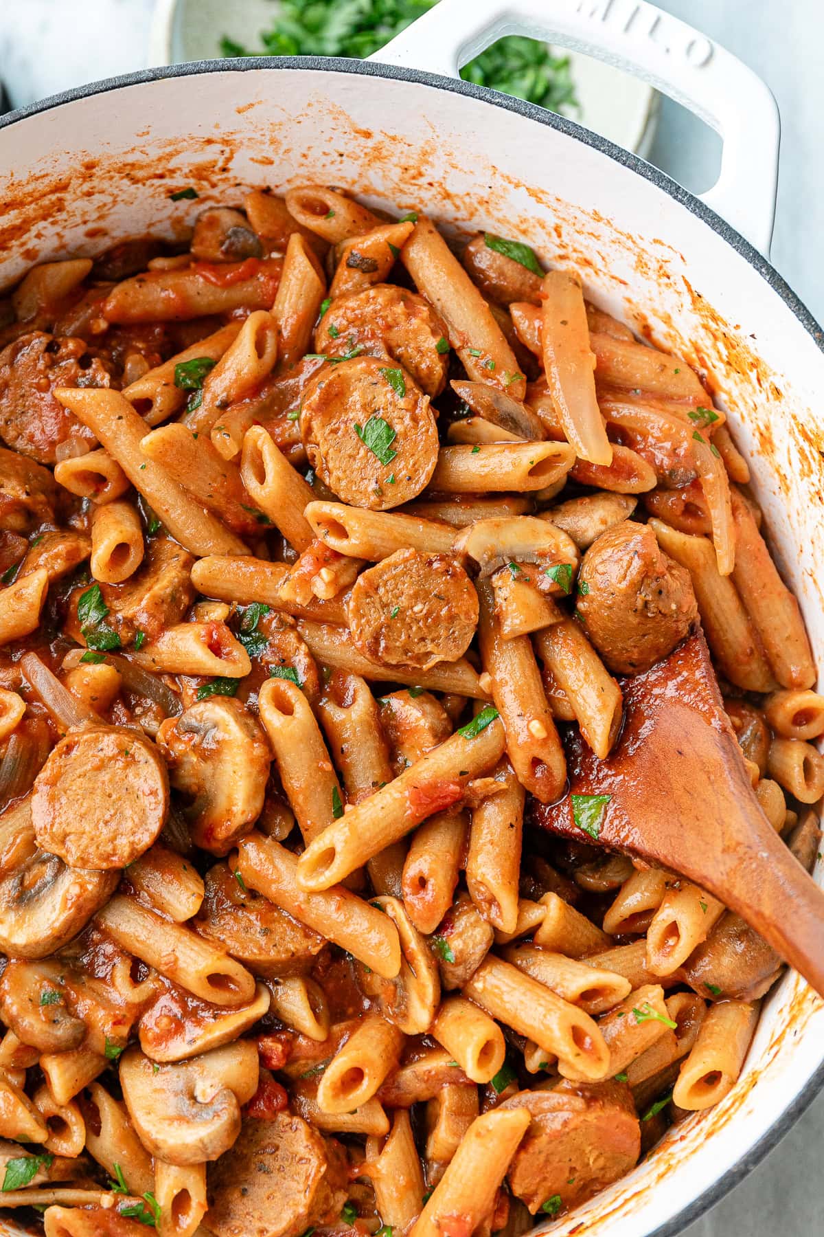 up close view of freshly made vegan sausage pasta in a white pot with wooden spoon.