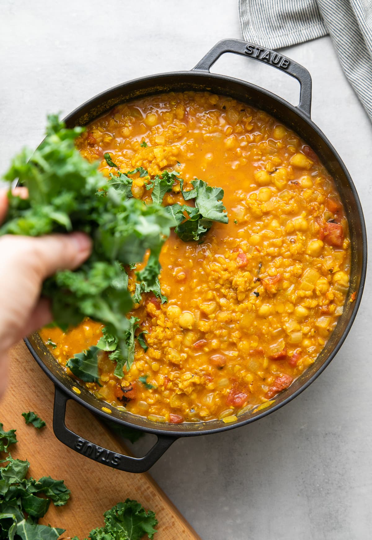 top down view of adding kale to curry red lentil stew in a black pot.