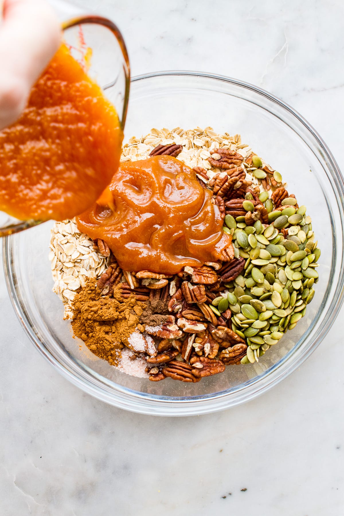 top down view showing the process of adding wet mixture to dry ingredients to make pumpkin granola.