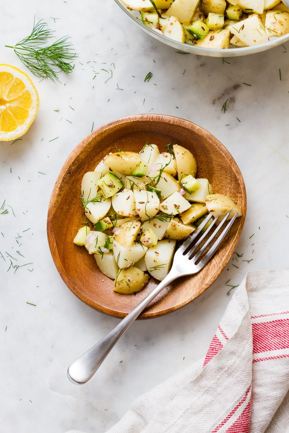 top down view of a small wooden plate with a serving of healthy vegan German potato salad with fork.