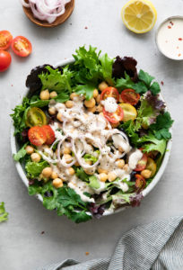 top down view of leafy green salad with chickpeas and dressed with lemony tahini dressing.