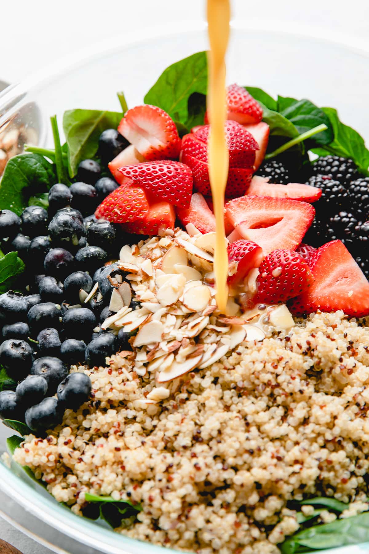 side angle view of orange dressing being poured over top berry spinach quinoa salad.
