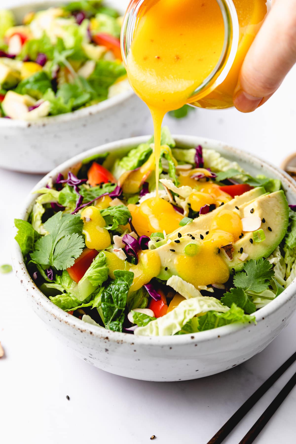 side angle view of mango dressing being poured over rainbow chop chop salad.
