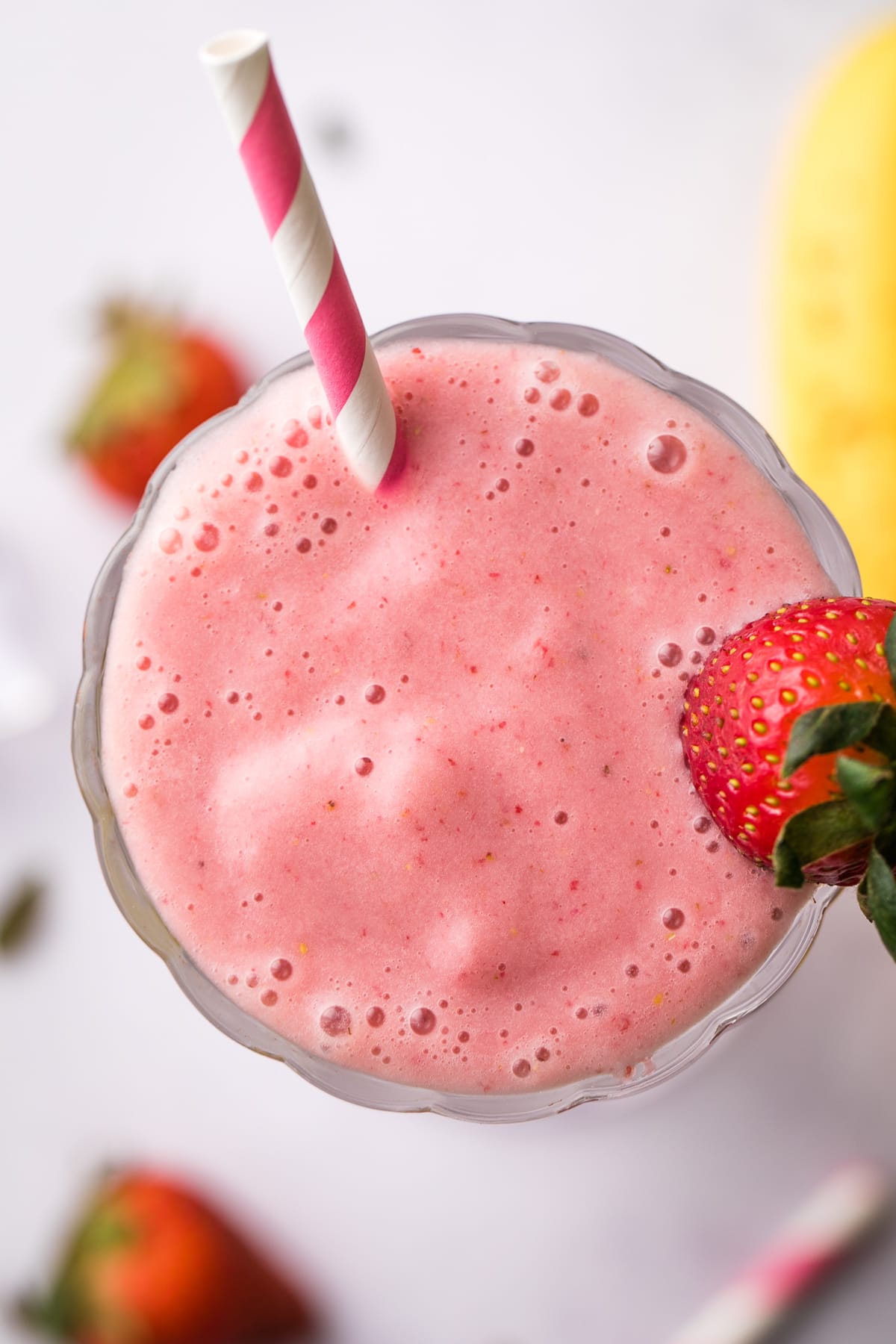 top down view of healthy vegan strawberry milkshake in a glass with items surrounding.