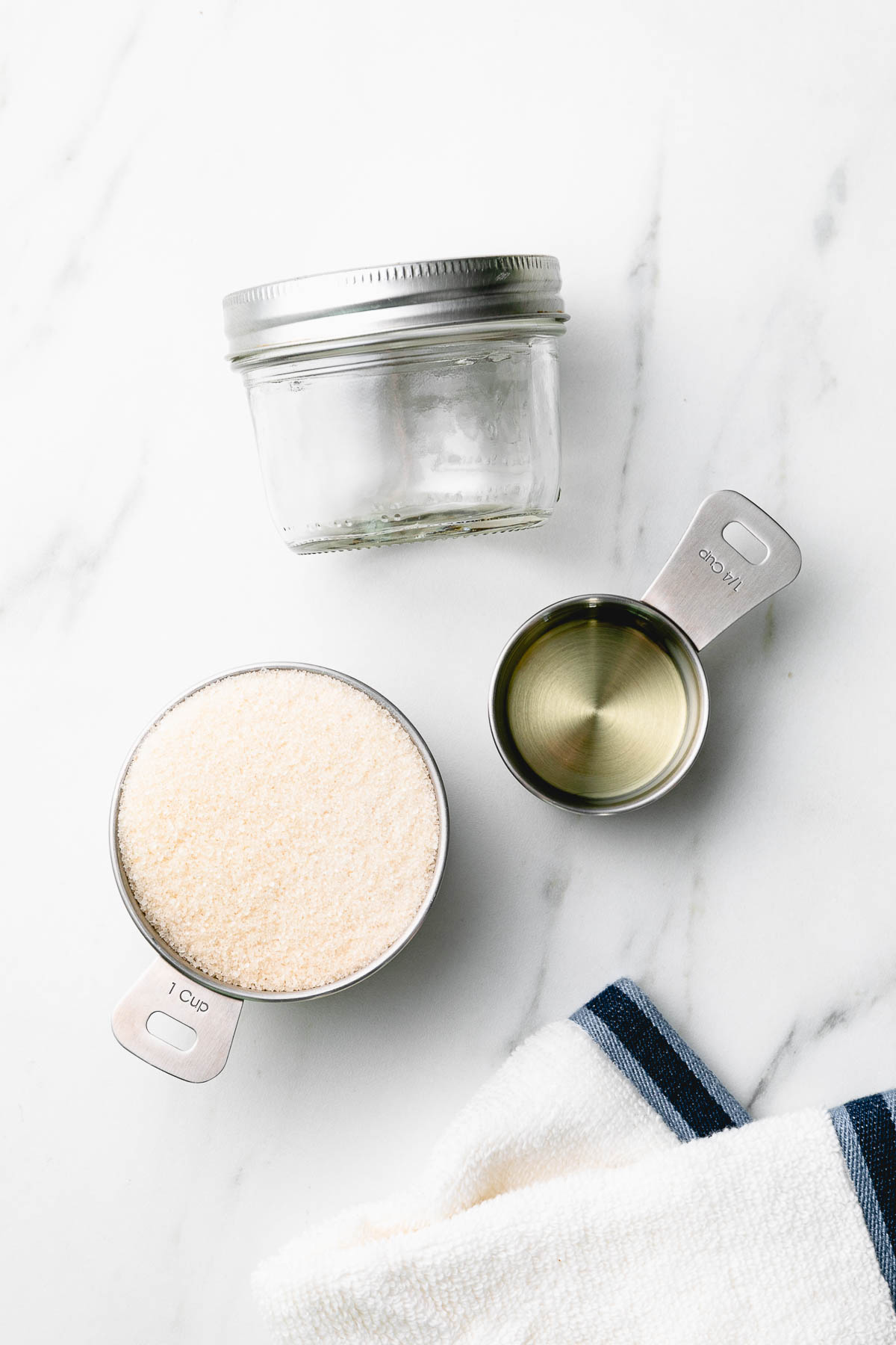 top down view of small glass ball jar, sugar and oil in measuring cups, and washcloth.