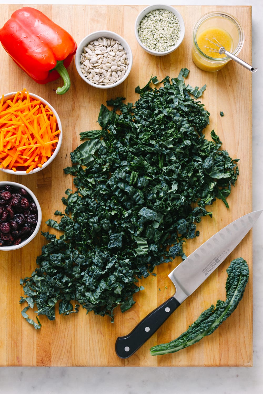 top down view of ingredients for kale salad with cranberries on a wooden cutting board.