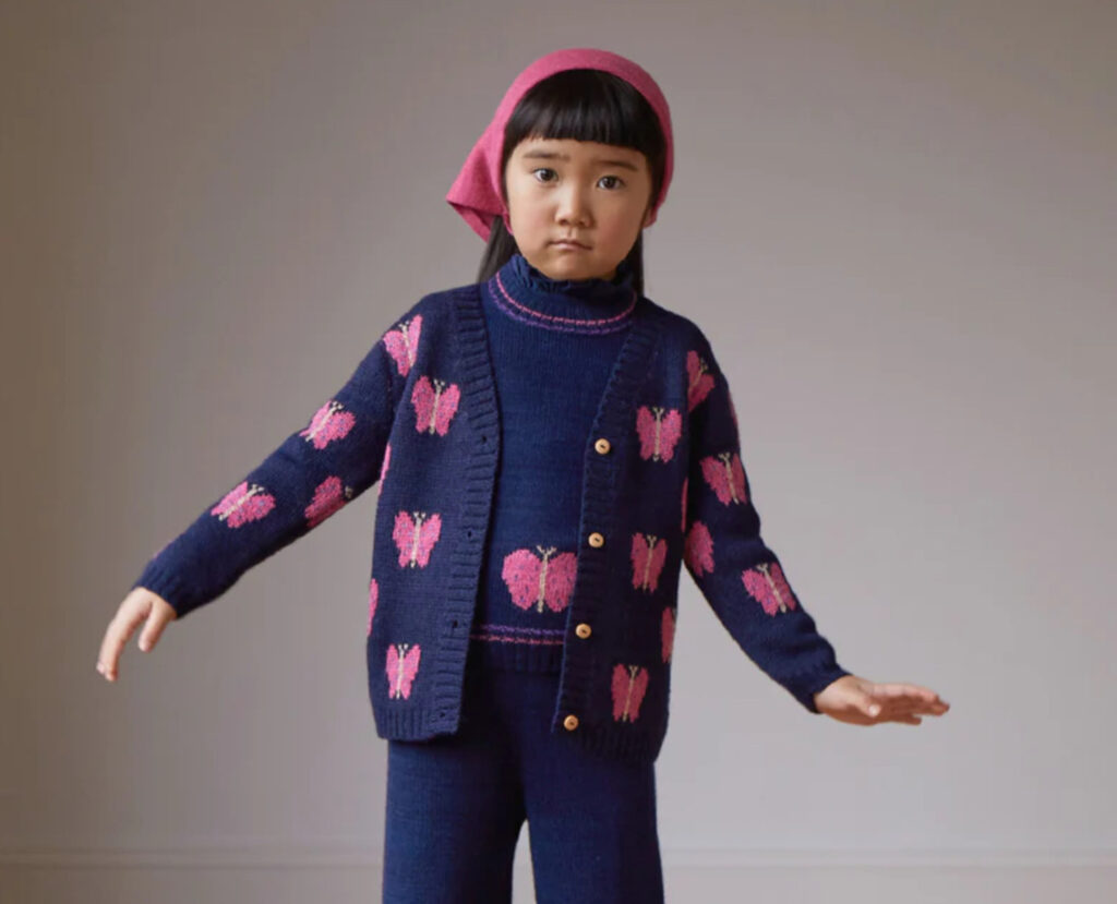 A young girl of 5 or 6 wears a navy knit outfit with a pink butterfly motif and a pink bandana over her dark hair.