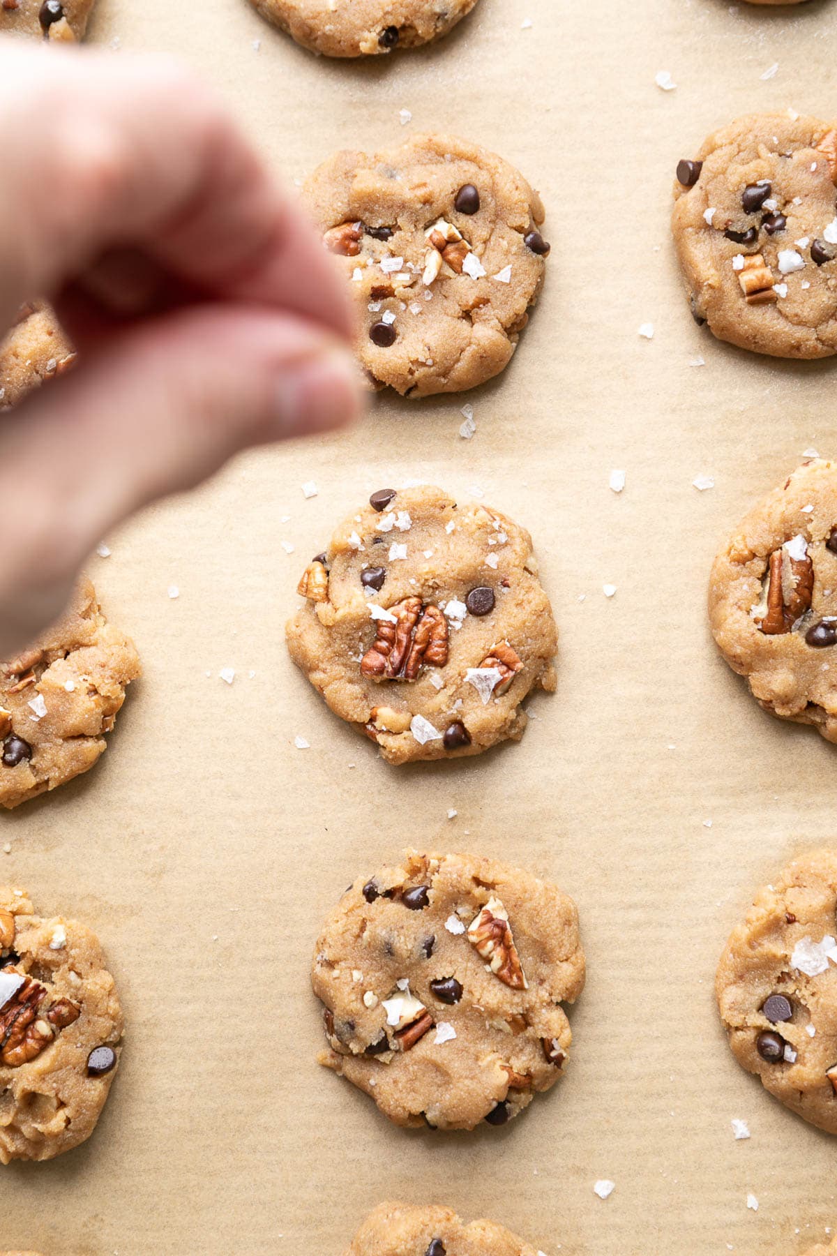 top down view of hand sprinkling pecan sandies with salt.