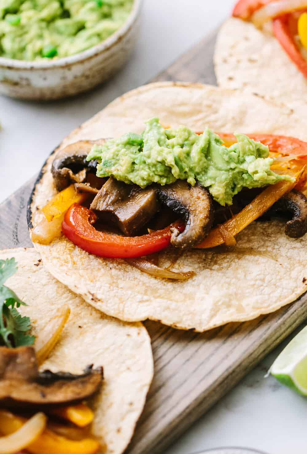 side angle view of easy portobello mushroom fajitas topped with jalapeno guacamole on corn tortillas.