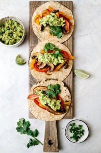top down view of easy portobello mushroom fajitas topped with jalapeno guacamole on corn tortillas on a wooden serving board.