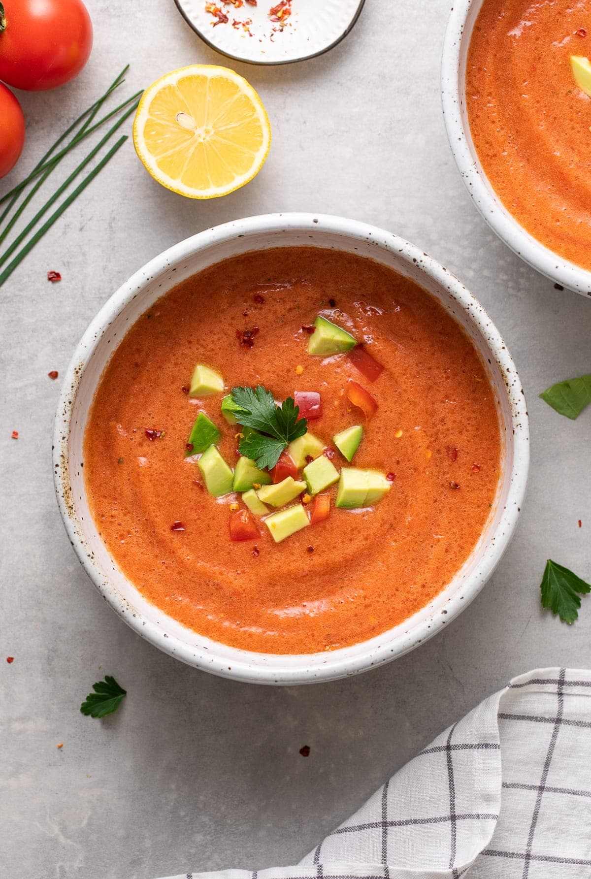 top down view of bowl with serving of spicy raw tomato soup with items surrounding.