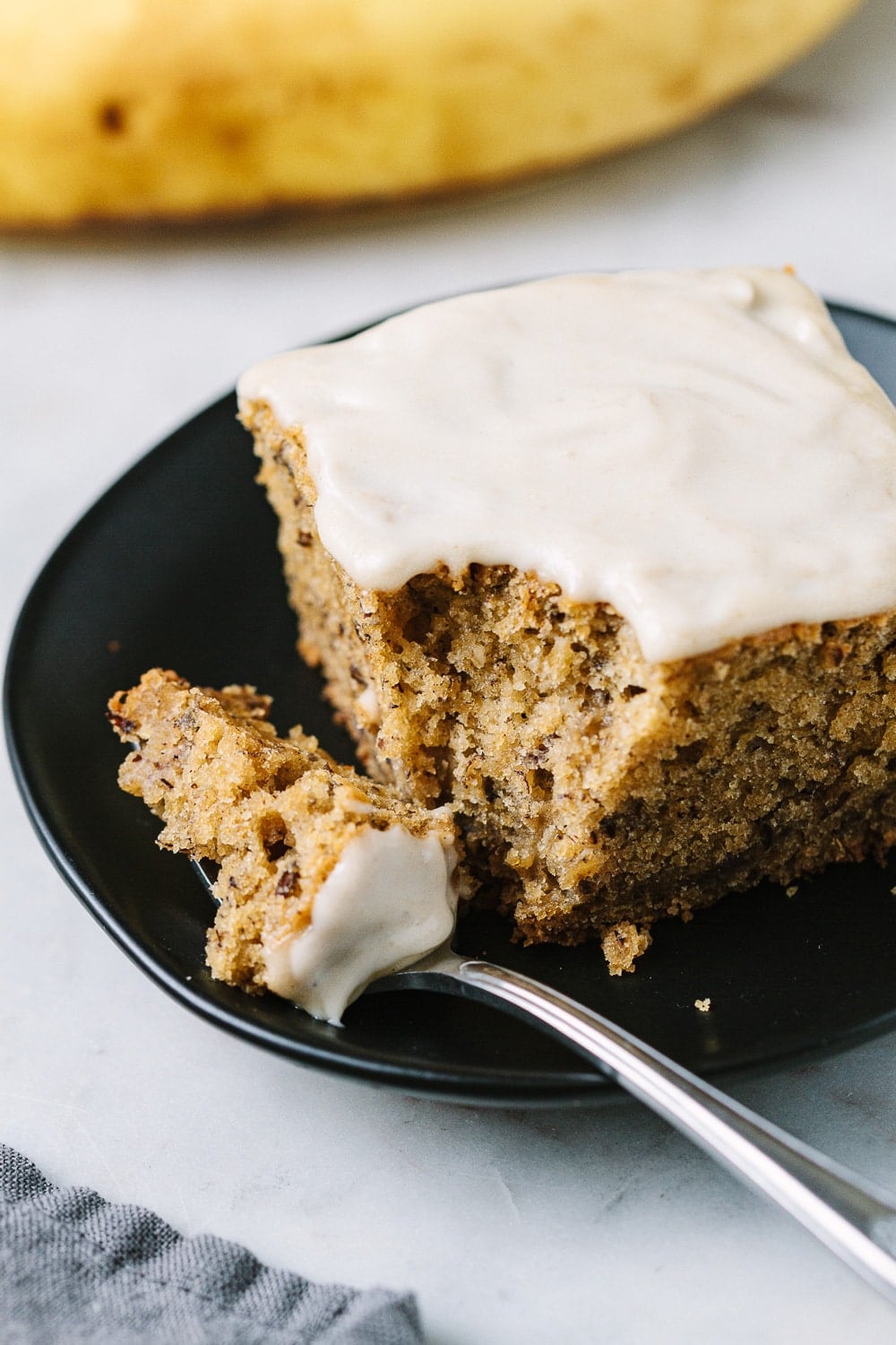 slice of vegan banana cake with a slice on a fork resting on a small black plate.