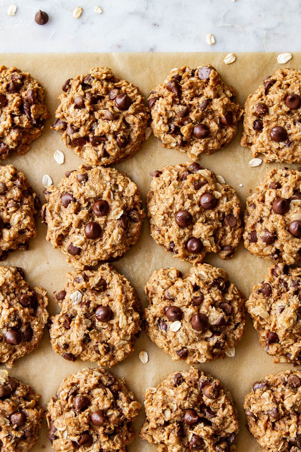 top down view of a batch of healthy vegan oatmeal chocolate chip cookies cooling on parchment paper.
